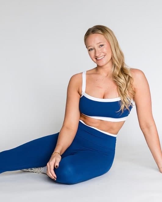 Dr. Julia, Doctor of Physical Therapy, sitting on a studio floor in athletic wear and smiling towards the camera.